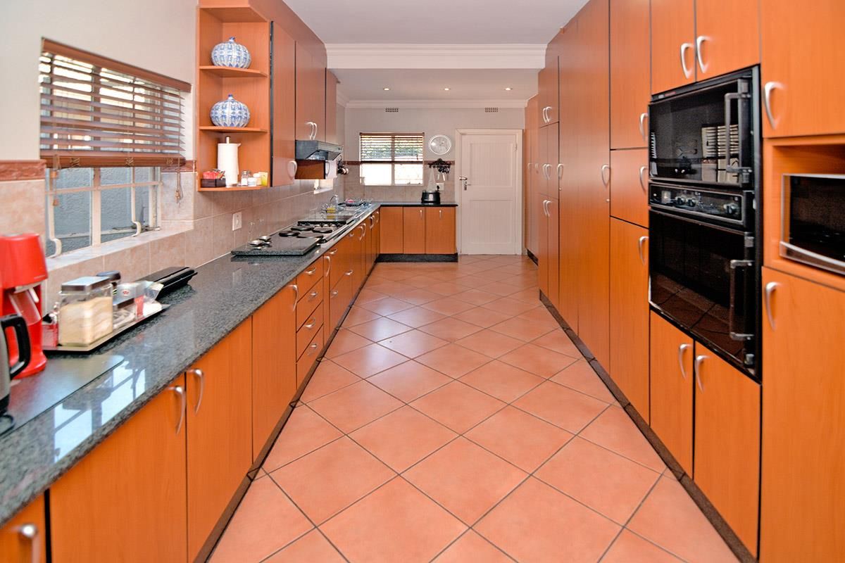 A spacious galley-style kitchen featuring extensive wood-veneer cabinetry, granite countertops, a built-in oven, and tiled flooring.