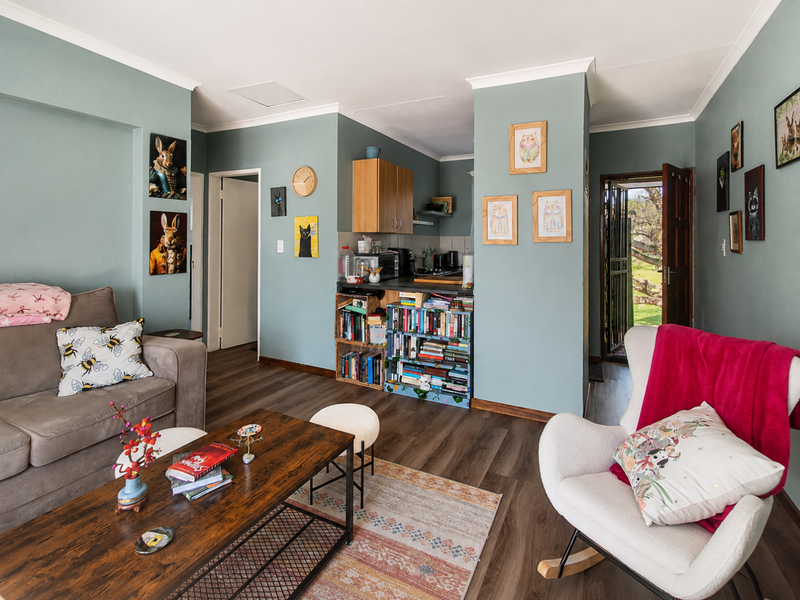 Open-plan living area featuring laminate flooring, coving, and a compact kitchen corner with built-in cabinetry, leading to an exterior entrance.