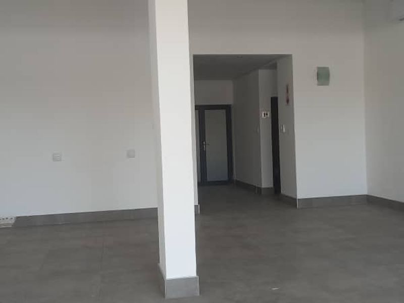 An empty open-plan retail space featuring tiled flooring, a central structural column, and neutral walls, ready for custom fit-out.