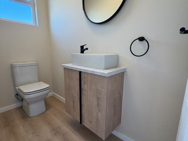A modern, minimalist bathroom featuring a floating wood-tone vanity, vessel sink with black fixtures, and light-toned laminate flooring.