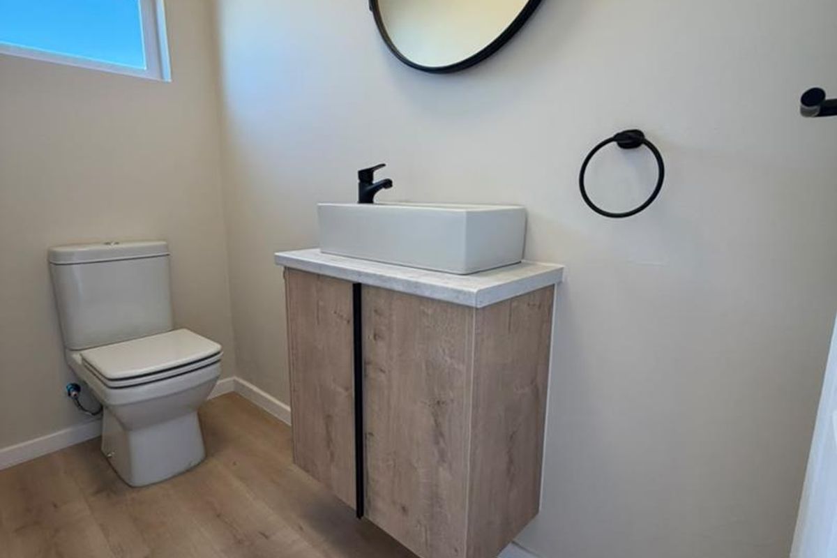A modern, minimalist bathroom featuring a floating wood-tone vanity, vessel sink with black fixtures, and light-toned laminate flooring.