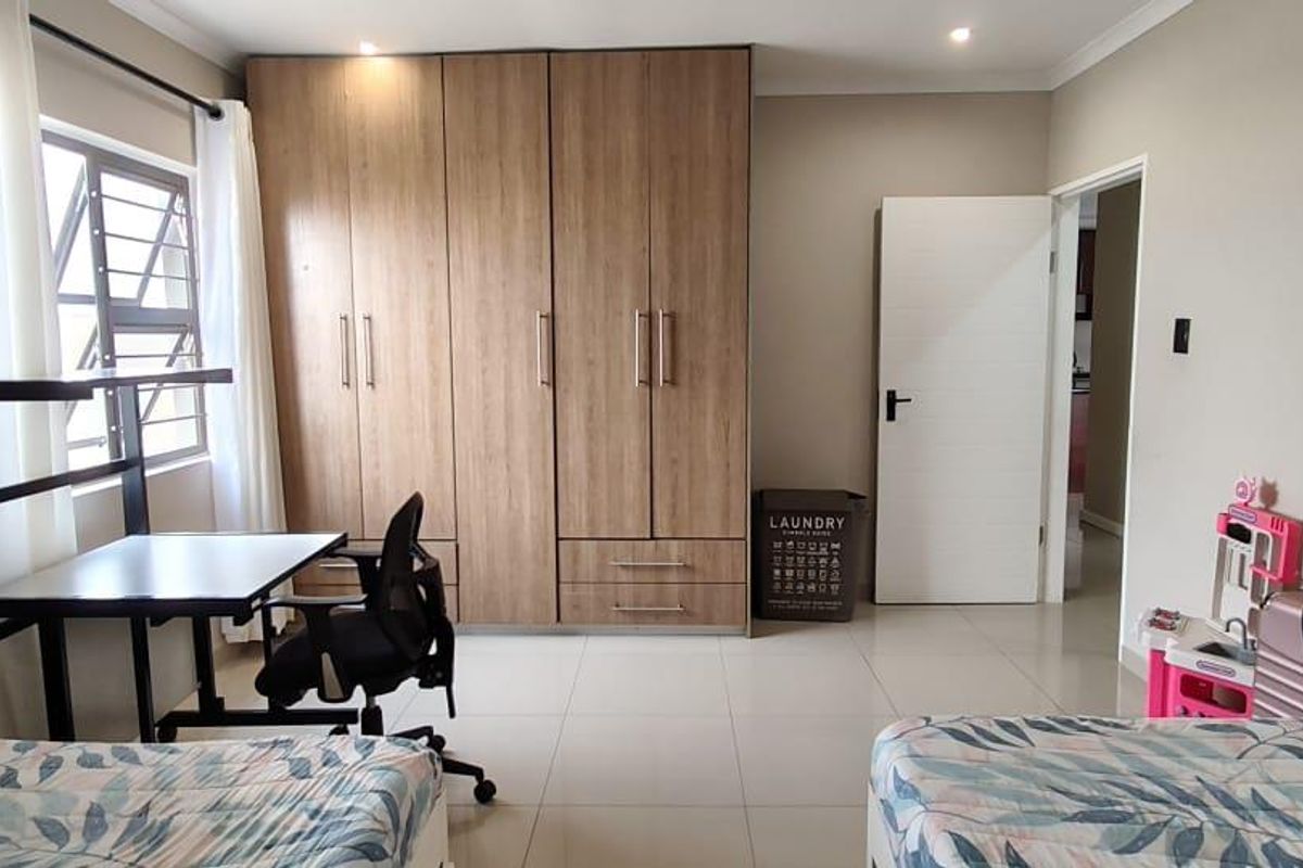 A well-maintained bedroom featuring neutral tiled flooring, recessed downlights, and ample built-in wooden cupboards for storage.
