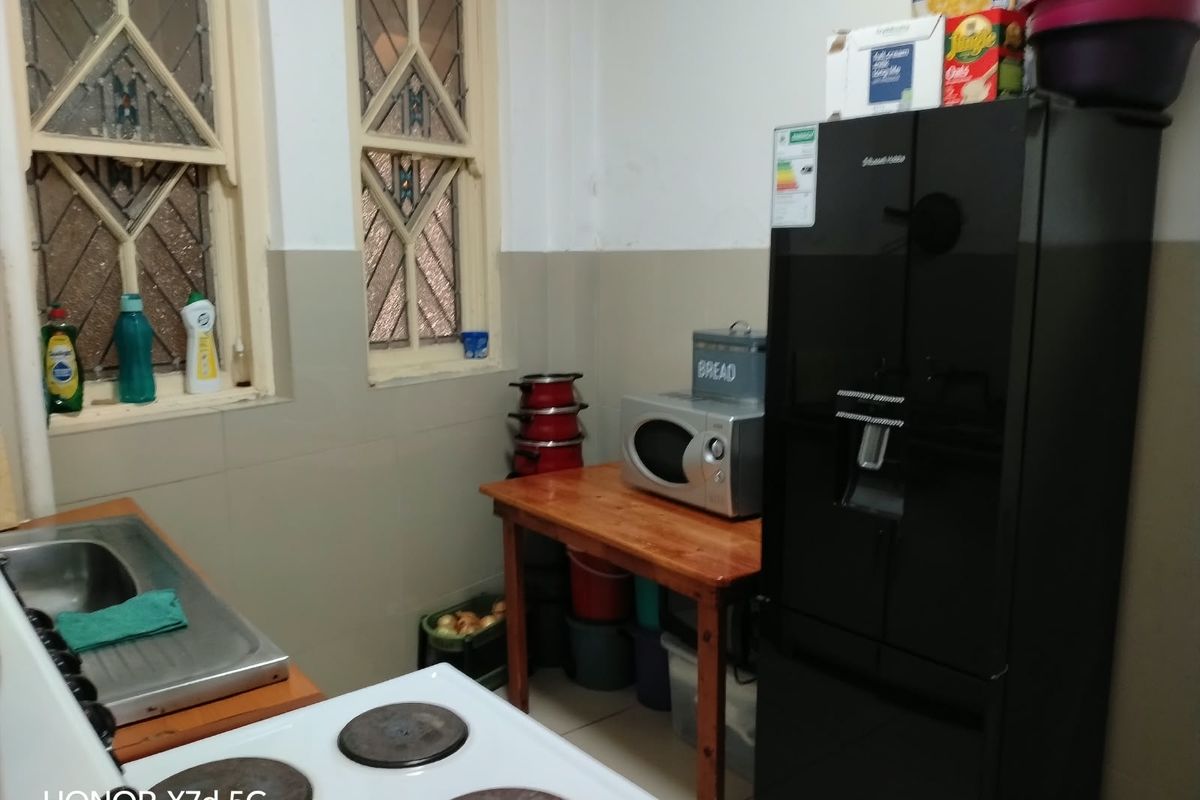 A compact kitchen featuring a stainless steel sink, electric stove, and classic leaded glass windows with neutral tiled splashbacks.