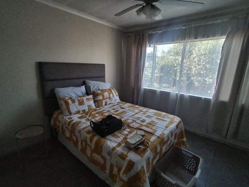 A functional bedroom featuring tiled flooring, a ceiling fan, and large windows allowing natural light.