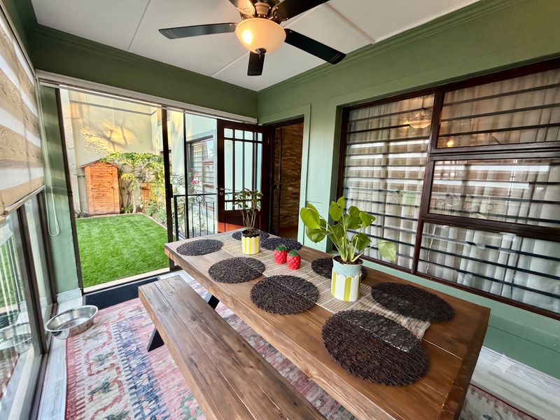 A covered patio area featuring a ceiling fan, sliding glass doors providing garden access, and secure window bars, creating a bright indoor-outdoor transition space.