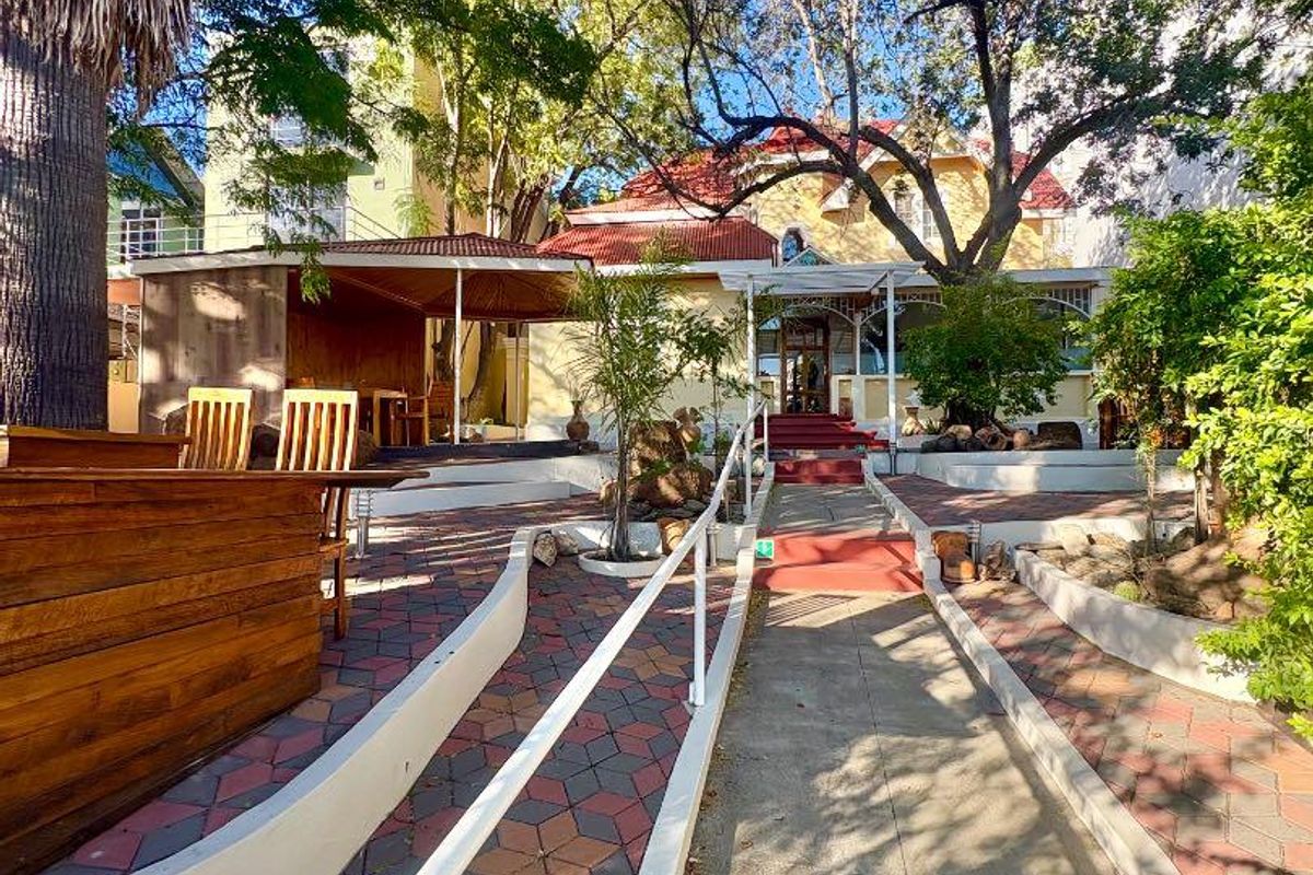Front entrance view of the office property featuring a paved walkway with handrails, landscaped garden, and a covered patio area.