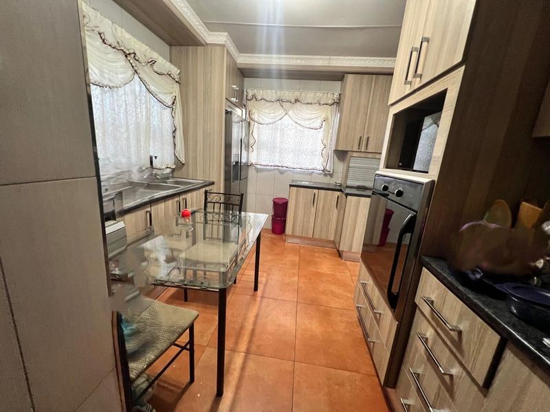 A functional kitchen featuring wood-look laminate cabinetry, built-in oven and microwave, double sink, and tiled flooring.