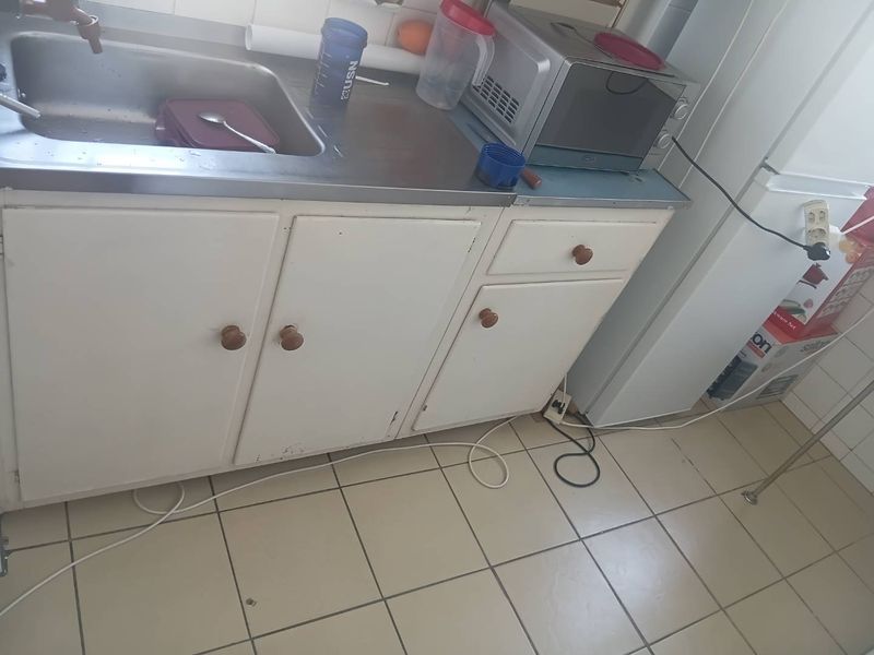 A compact kitchen area featuring a stainless steel sink, built-in cabinetry, and tiled flooring, requiring cosmetic updates to improve its overall condition.