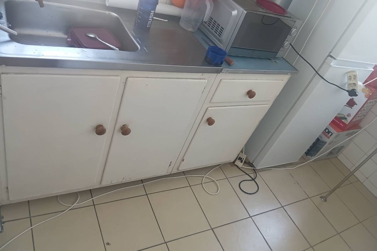 A compact kitchen area featuring a stainless steel sink, built-in cabinetry, and tiled flooring, requiring cosmetic updates to improve its overall condition.
