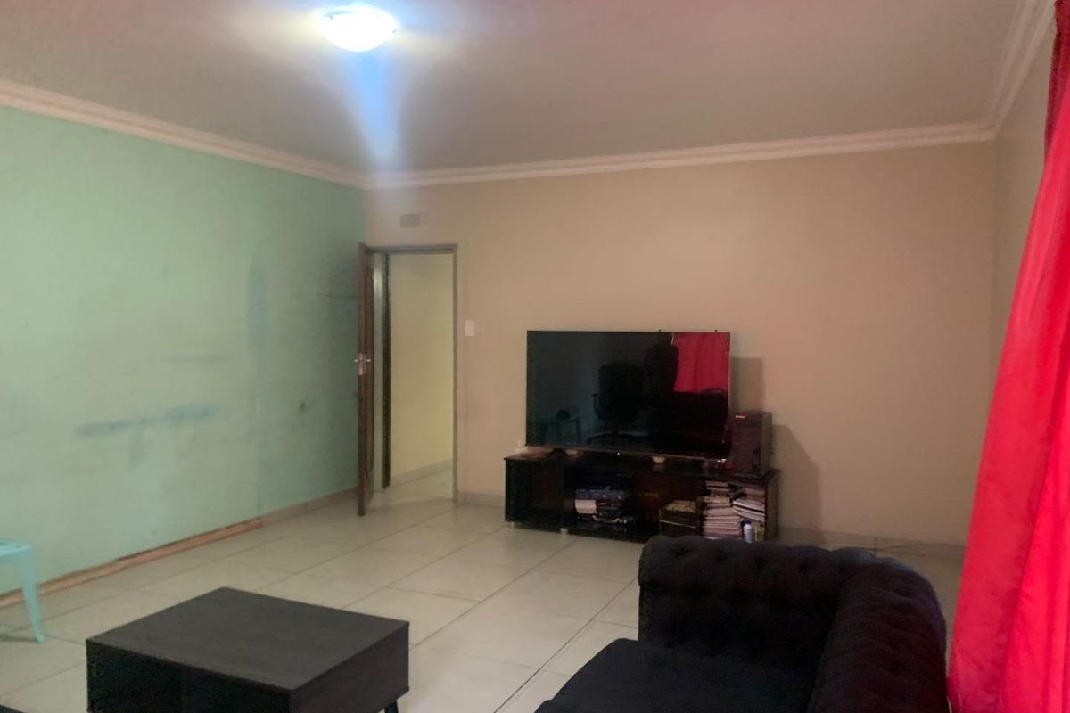 A living room featuring tiled flooring and ceiling cornice, currently requiring cosmetic updates to the wall finishes and baseboards.