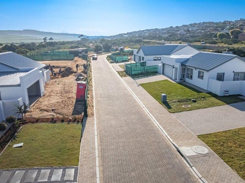 Aerial view of a modern residential street featuring paved driveways, manicured lawns, and contemporary homes with metal roofing in a developing estate.