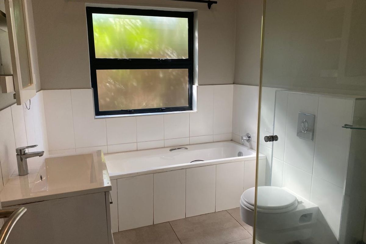 A clean, modern bathroom featuring a built-in bathtub, wall-mounted toilet, vanity basin, and a glass shower screen with neutral tiling.