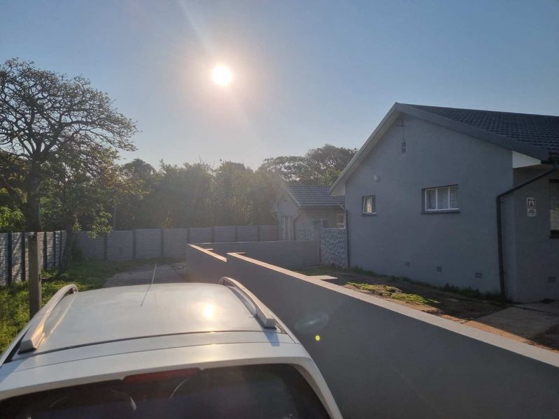 Rear view of the property featuring a plastered exterior, tiled roof, and a concrete boundary wall enclosing the yard area.