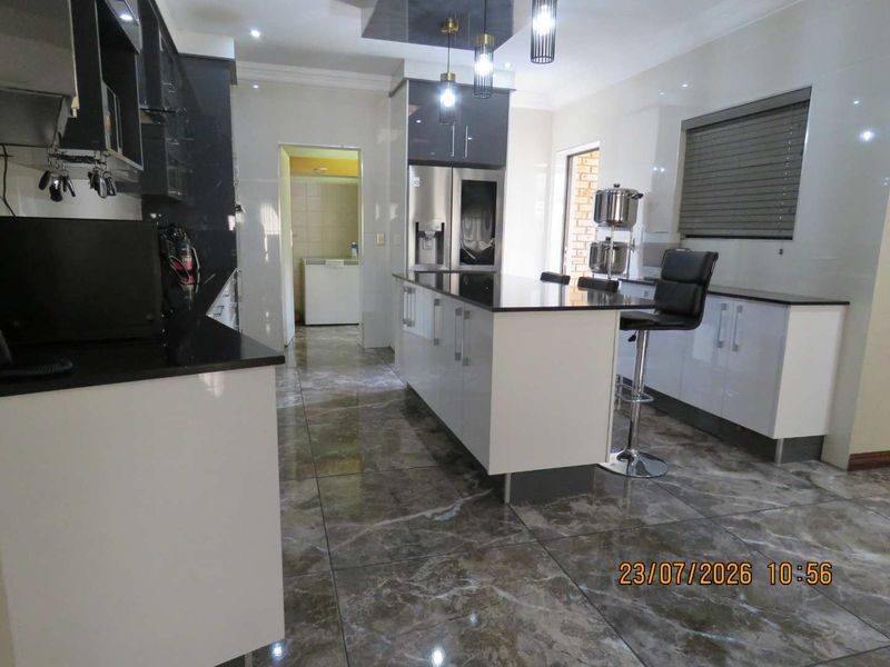 Modern kitchen featuring a central island, high-gloss cabinetry, granite countertops, and polished tiled flooring with integrated lighting.