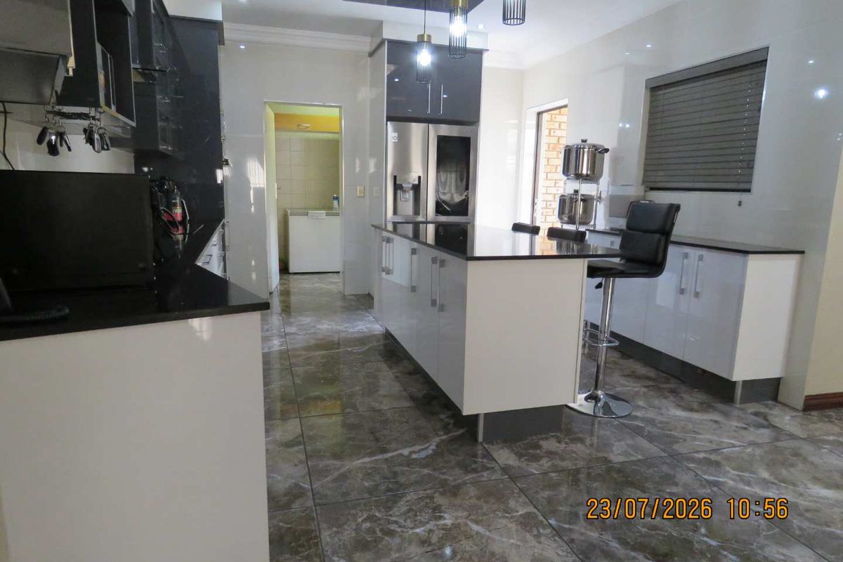 Modern kitchen featuring a central island, high-gloss cabinetry, granite countertops, and polished tiled flooring with integrated lighting.