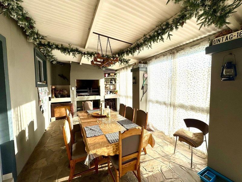 Covered patio area featuring a built-in braai, stone flooring, and a corrugated roof, providing a functional space for outdoor dining and entertainment.