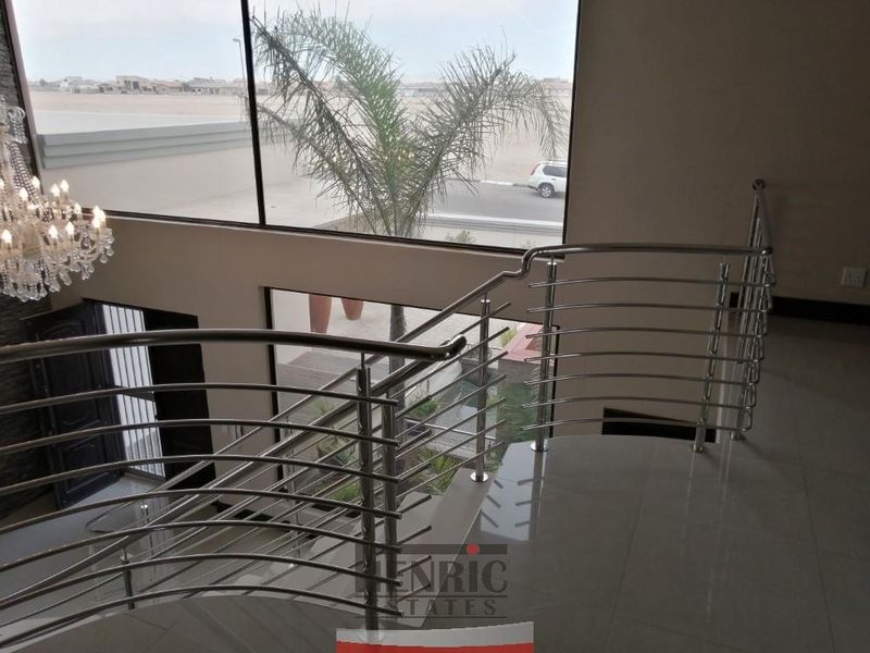 A bright, double-volume landing area featuring modern stainless steel balustrades and expansive windows overlooking the exterior.