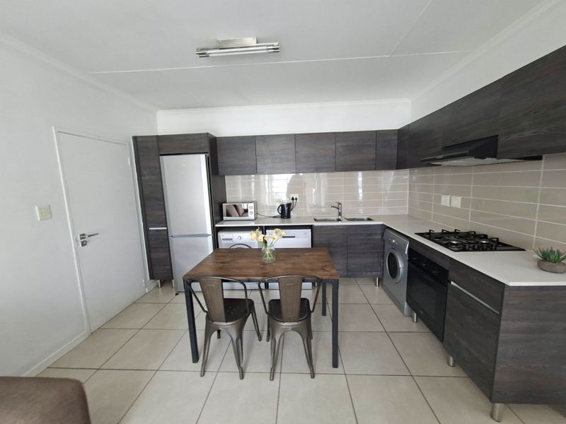 Modern kitchen featuring dark wood-finish cabinetry, white countertops, gas hob, integrated oven, and tiled flooring with a functional layout.