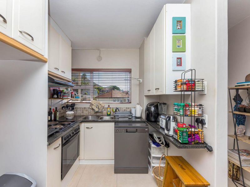 Compact kitchen featuring built-in cabinetry, stone countertops, integrated oven and hob, tiled backsplash, and a window providing natural light.