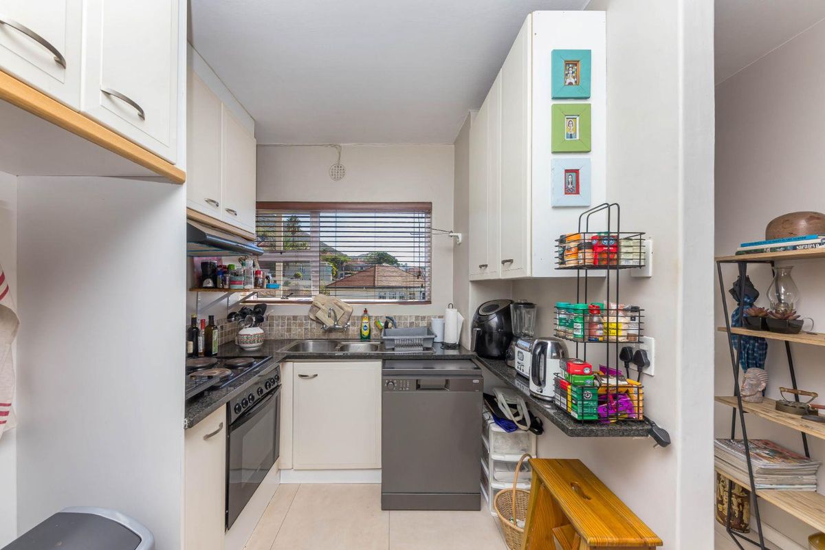 Compact kitchen featuring built-in cabinetry, stone countertops, integrated oven and hob, tiled backsplash, and a window providing natural light.