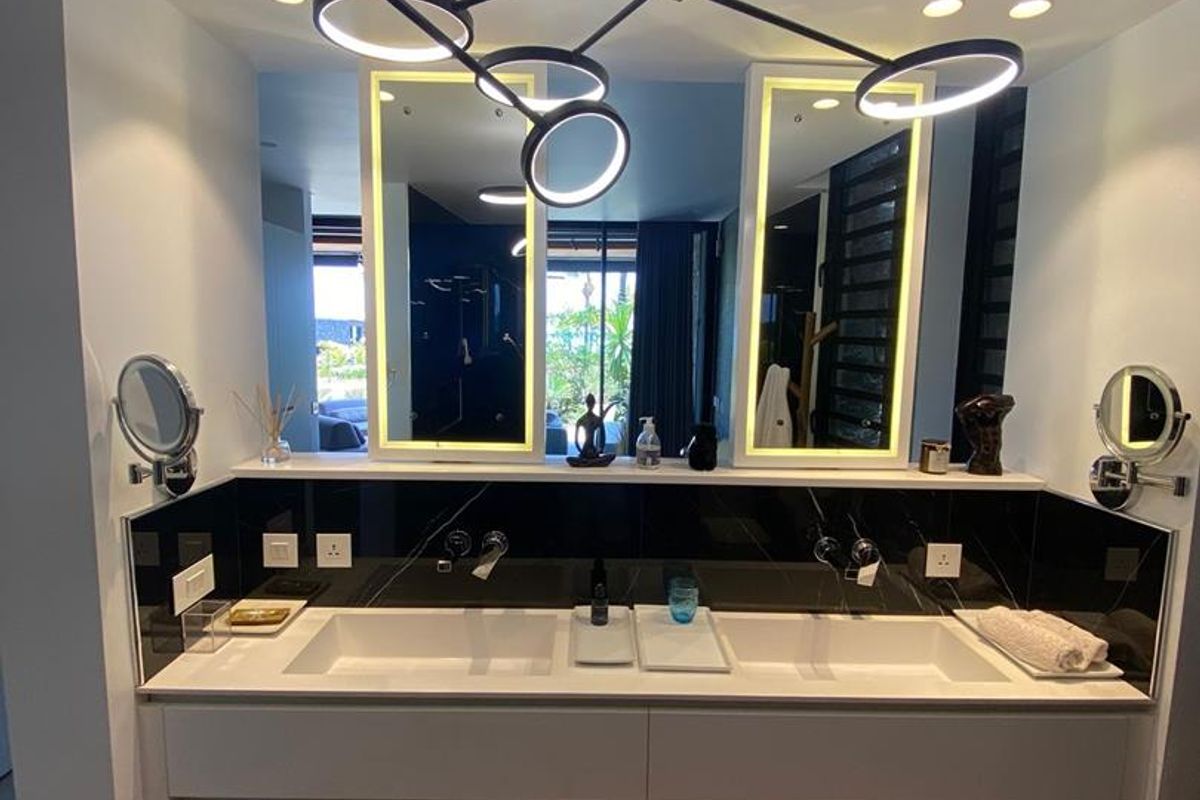 Modern bathroom vanity featuring a double sink, sleek white cabinetry, black marble backsplash, and contemporary circular pendant lighting.