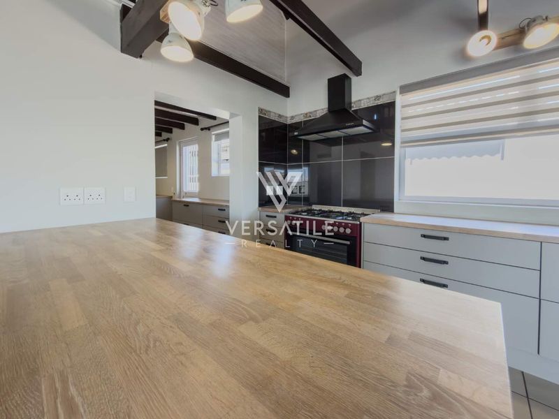 Modern kitchen featuring a large wooden countertop, sleek cabinetry, gas stove with extractor fan, and exposed ceiling beams, offering a clean and functional workspace.