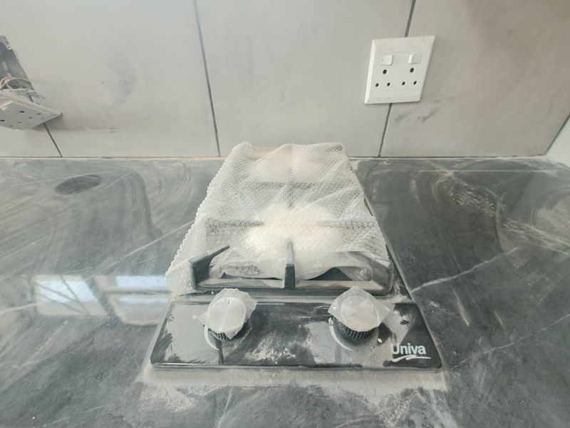 A newly installed gas hob set into a stone countertop with tiled splashback, currently undergoing final finishing and cleaning.