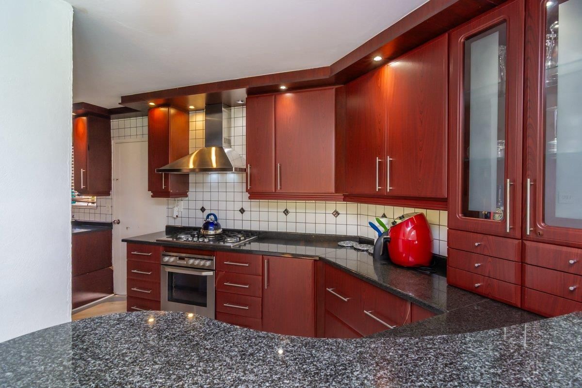 A functional kitchen featuring dark wood cabinetry, granite countertops, a stainless steel gas stove, and a built-in extractor fan.