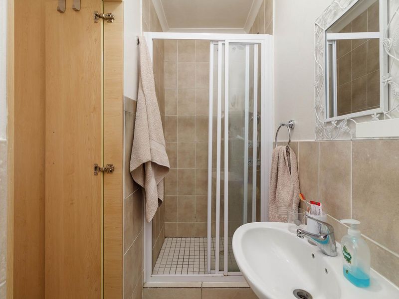 A functional bathroom featuring a tiled shower enclosure with a sliding door, a pedestal basin with a chrome mixer tap, and built-in storage.