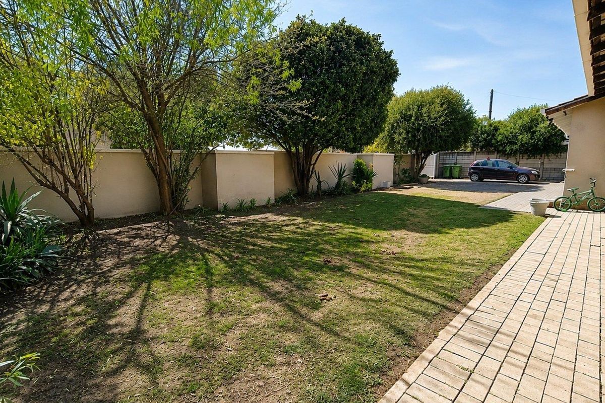 A rear garden area featuring a paved walkway, boundary wall, and a lawn with mature trees.