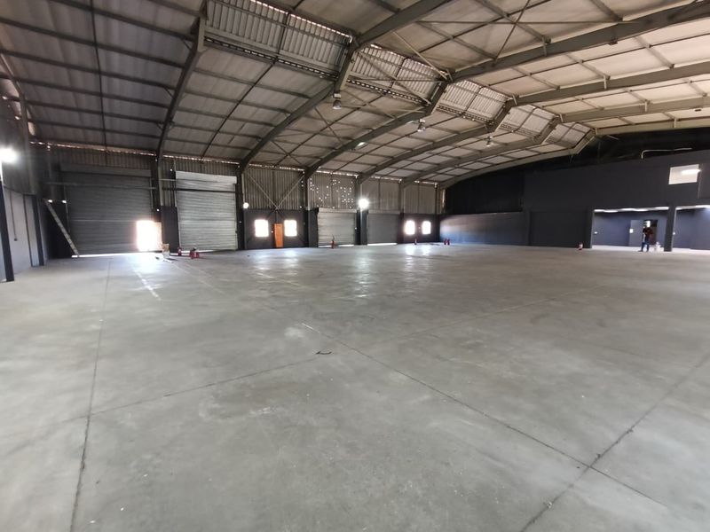 Spacious industrial warehouse featuring high ceilings, concrete flooring, and multiple roller shutter doors, suitable for storage, manufacturing, or logistics operations.
