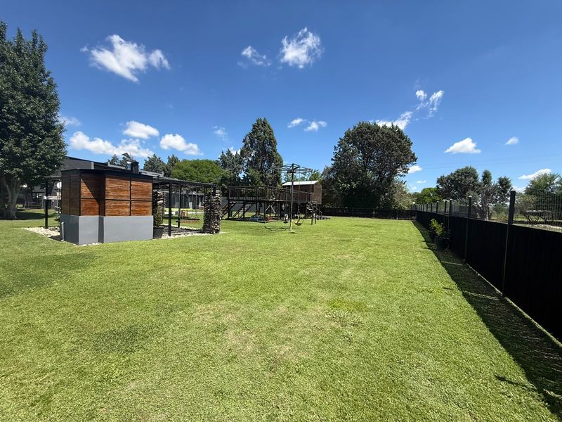 A spacious, well-maintained garden featuring a large lawn, perimeter fencing, and a wooden outdoor structure.