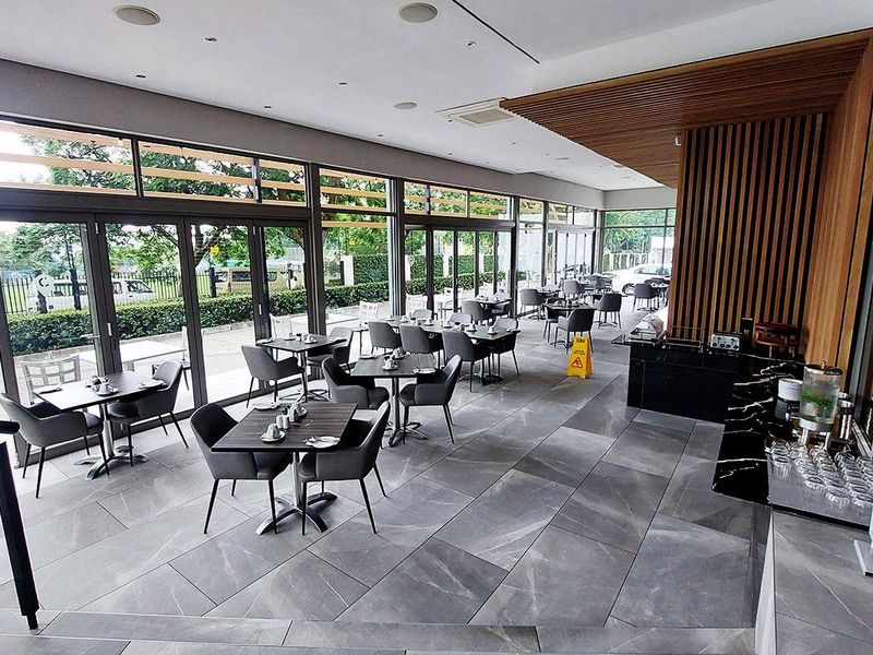 Modern open-plan dining area featuring large format floor tiles, floor-to-ceiling glass doors, and a sophisticated timber slat feature wall with integrated lighting.