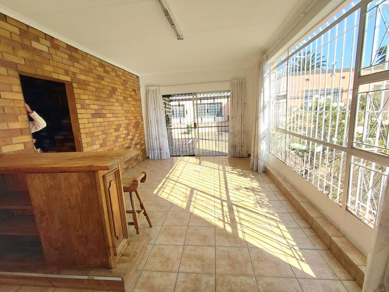 A sunlit living area featuring a brick accent wall, tiled flooring, and a built-in bar counter, with direct access to the outdoor space.
