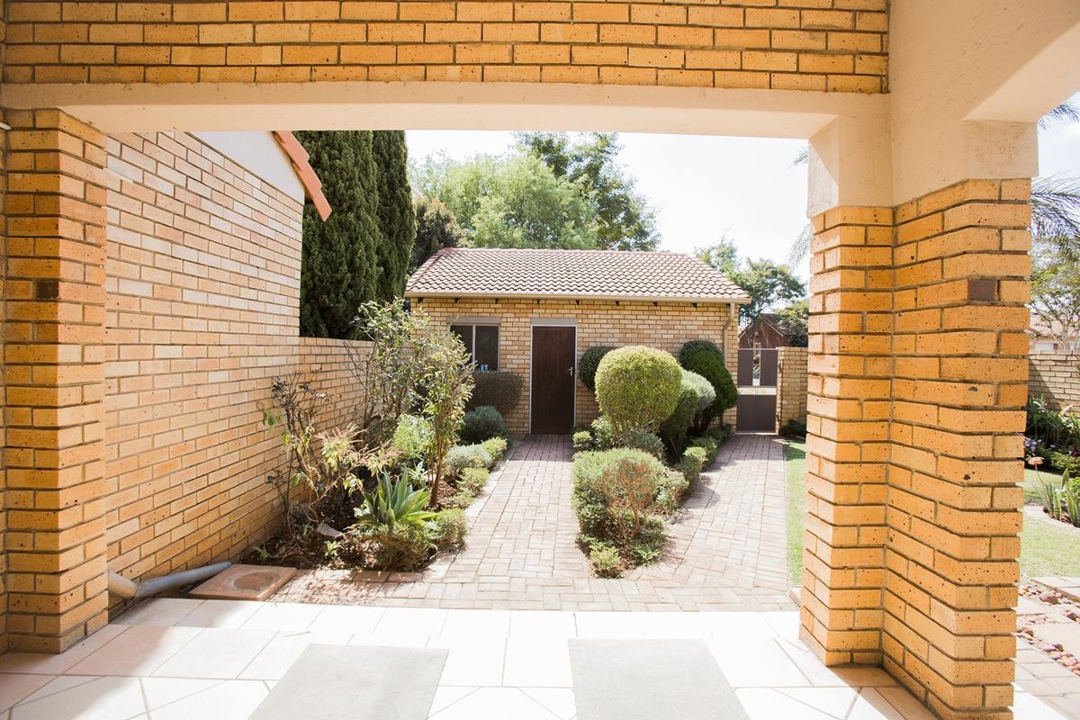 A view from a covered patio looking out onto a landscaped garden path leading to a detached brick outbuilding.