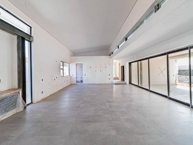 Spacious, light-filled open-plan living area featuring large format floor tiles, expansive sliding glass doors, and modern clerestory windows in a contemporary unfinished state.