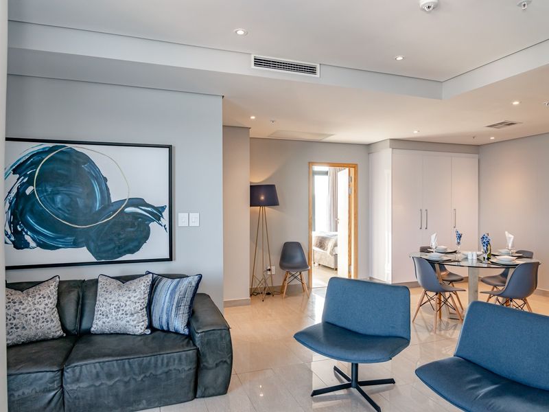 A modern open-plan living and dining area featuring neutral tiled flooring, recessed lighting, ducted air conditioning, and built-in storage cupboards.