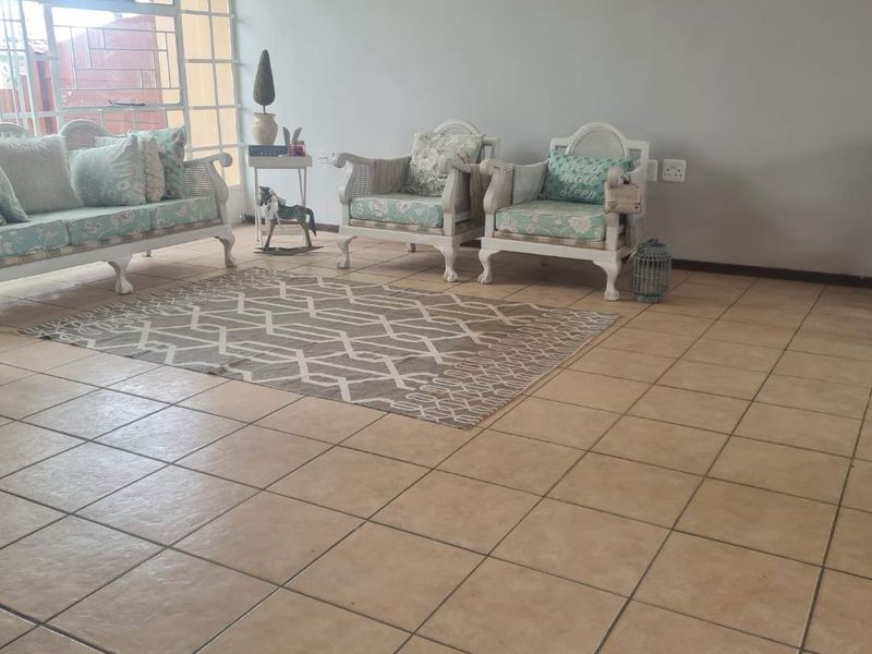 A living room area featuring neutral tiled flooring and a large window with security bars, providing natural light to the space.