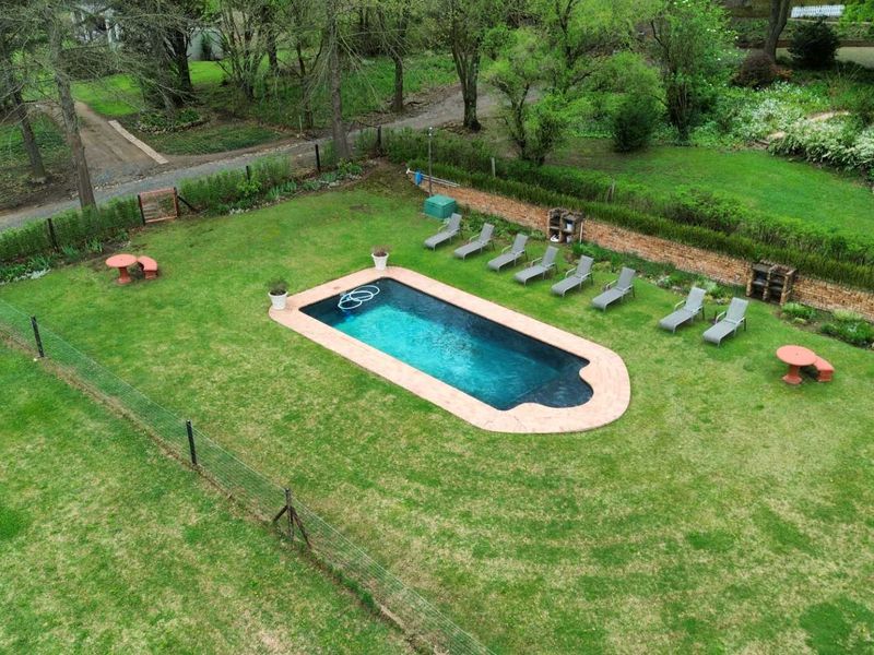 Aerial view of a residential swimming pool set within a spacious, well-maintained garden with perimeter fencing and a brick retaining wall.