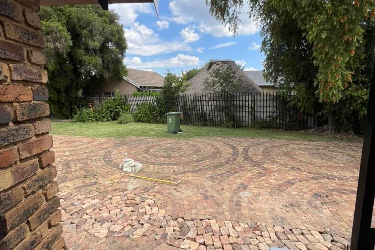 A view of the rear garden featuring a circular patterned brick paved patio area and established trees.