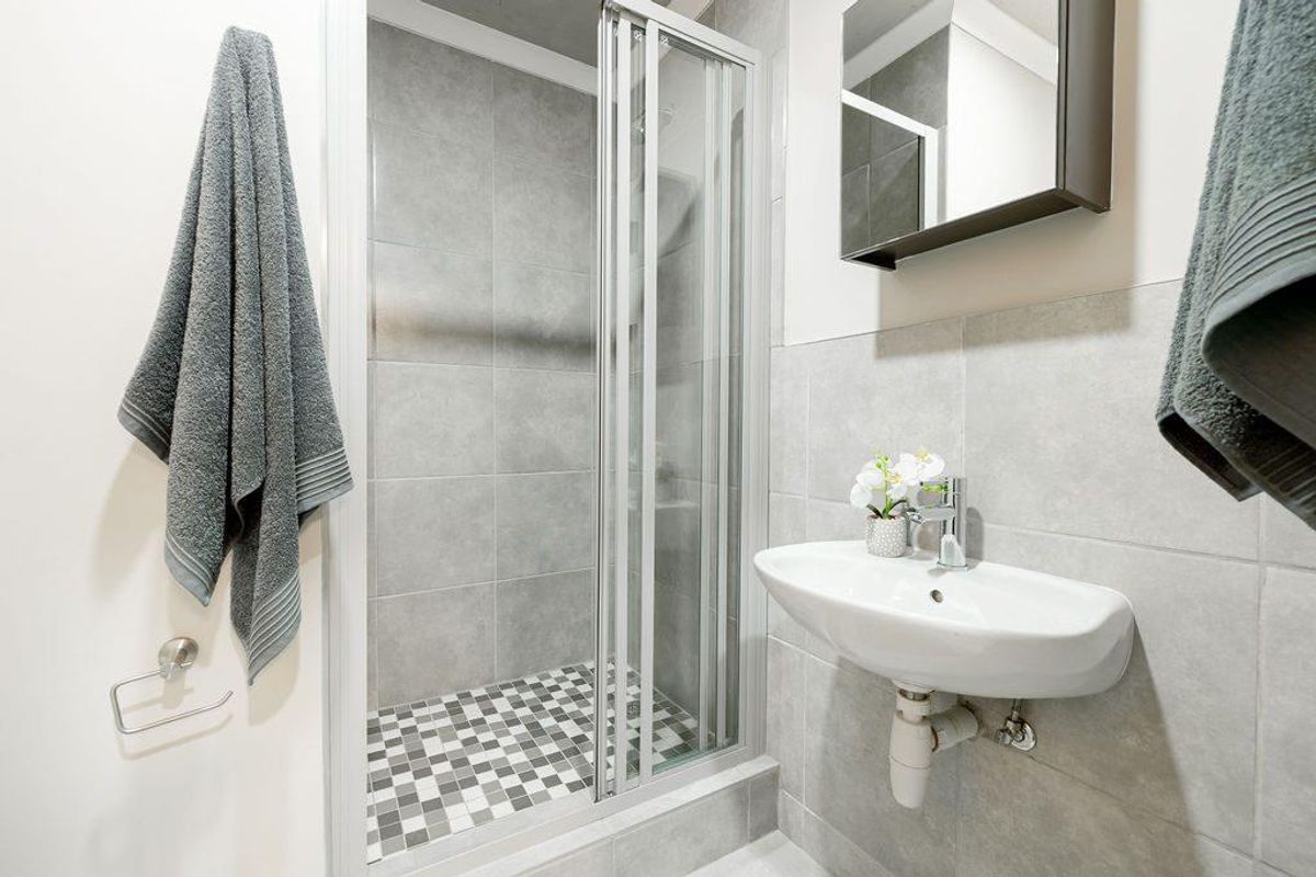 Modern bathroom featuring a glass-enclosed shower with mosaic floor tiling, a wall-mounted basin, and a mirrored medicine cabinet.