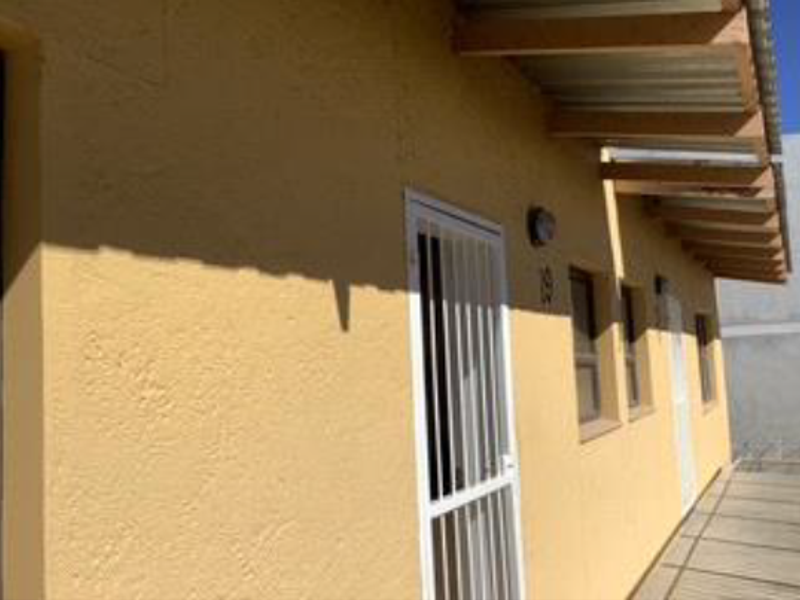 Exterior view of the apartment facade featuring a security gate, exposed timber rafters, and corrugated metal roofing.