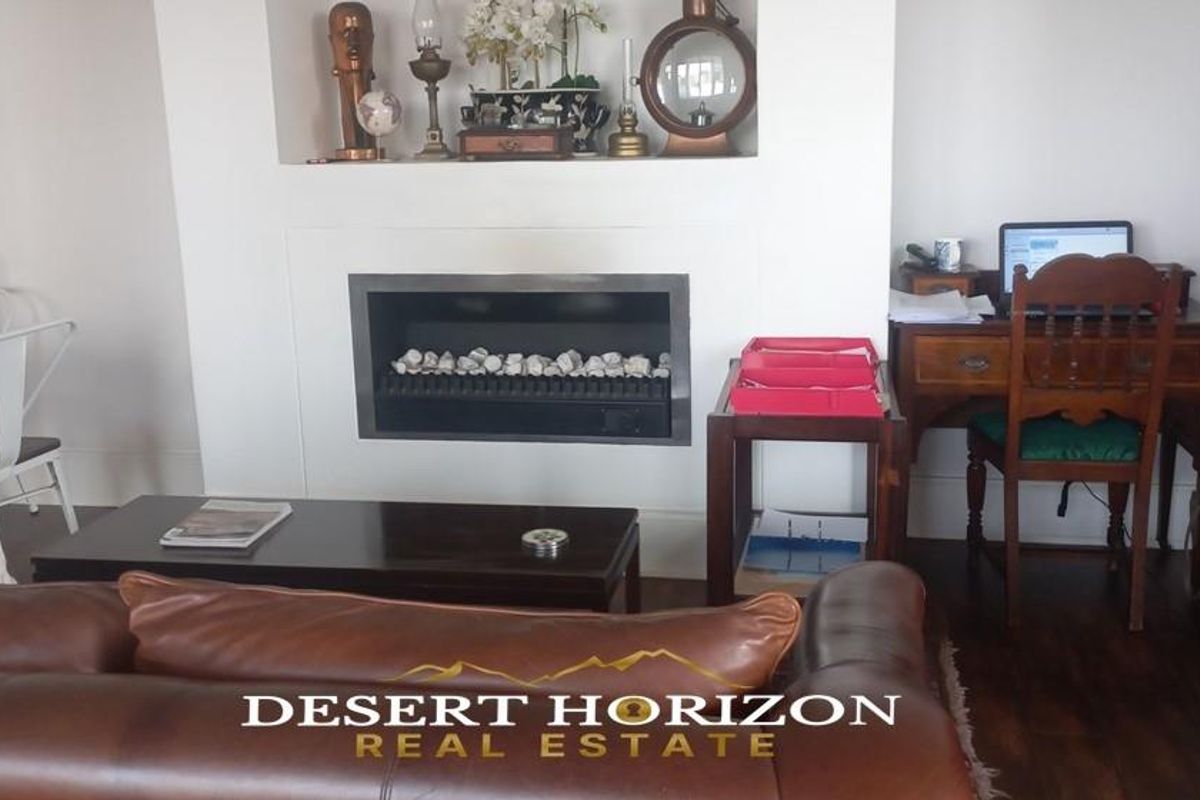 A comfortable living room featuring a built-in fireplace with a recessed display niche above, set against a neutral backdrop with dark wood flooring.
