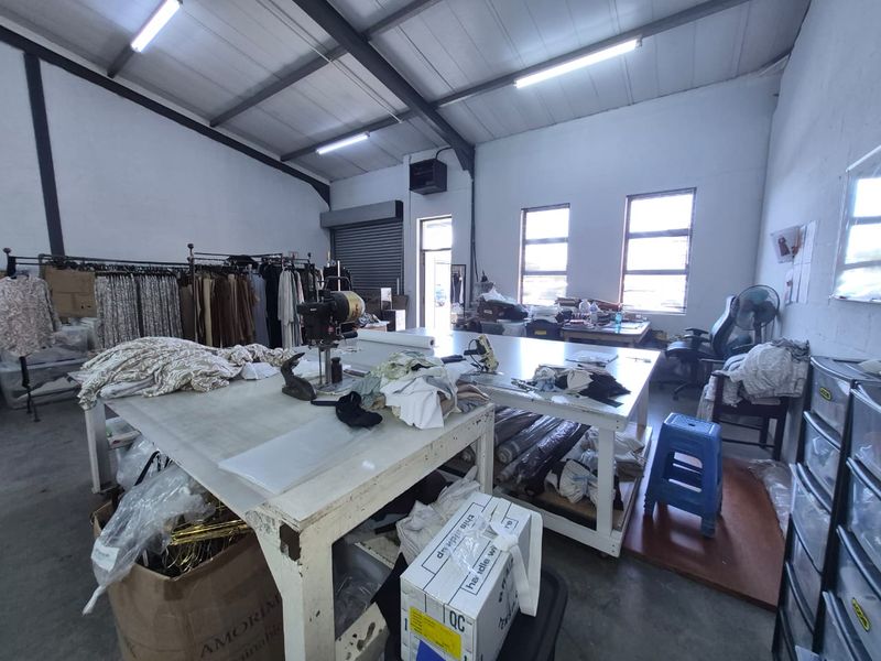 Industrial workspace featuring high ceilings with exposed steel trusses, concrete flooring, and a roller shutter door, suitable for manufacturing or storage operations.