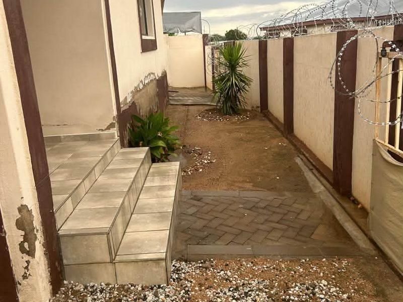 Side exterior area of the townhouse featuring tiled steps, a paved walkway, and a boundary wall secured with razor wire.