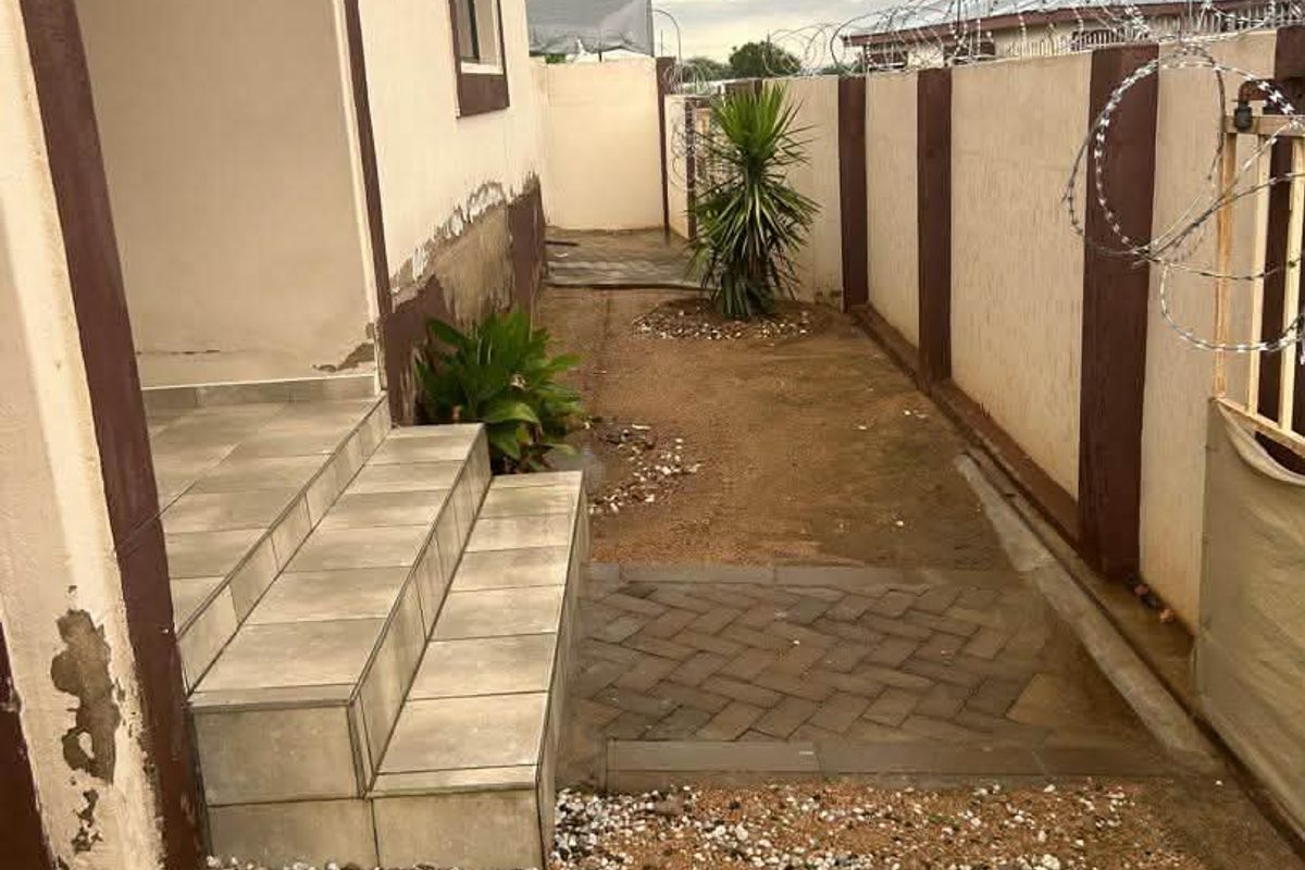 Side exterior area of the townhouse featuring tiled steps, a paved walkway, and a boundary wall secured with razor wire.