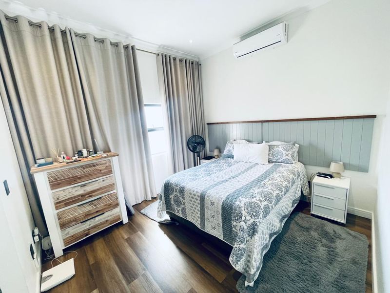 A well-maintained bedroom featuring laminate flooring, a wall-mounted air conditioning unit, and decorative timber wall panelling behind the bed area.