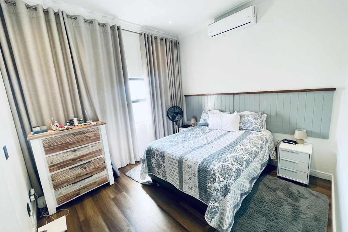 A well-maintained bedroom featuring laminate flooring, a wall-mounted air conditioning unit, and decorative timber wall panelling behind the bed area.