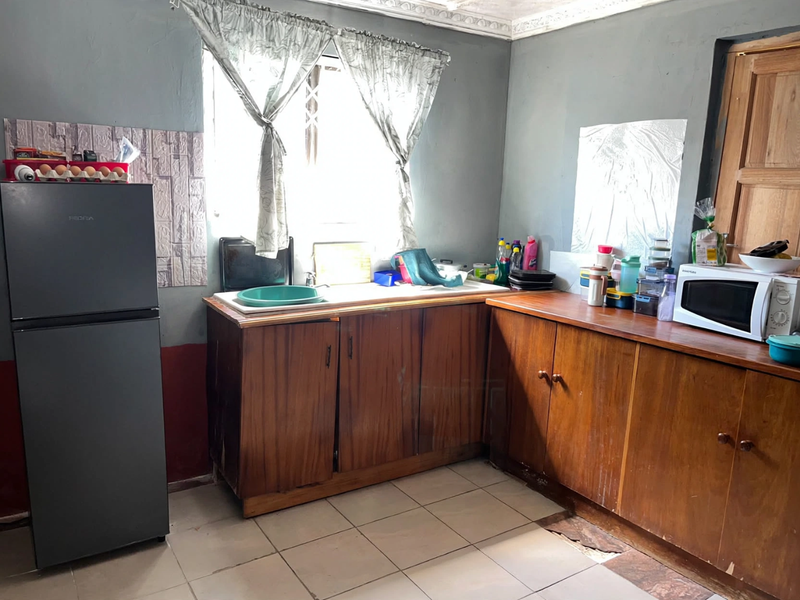 A functional kitchen featuring wooden cabinetry, tiled flooring, and a sink, currently showing signs of wear and requiring cosmetic updates.