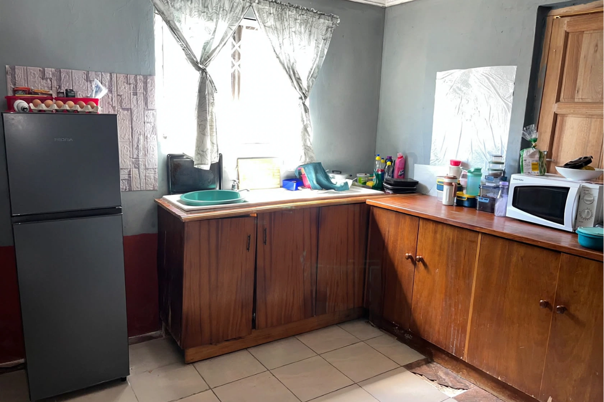 A functional kitchen featuring wooden cabinetry, tiled flooring, and a sink, currently showing signs of wear and requiring cosmetic updates.